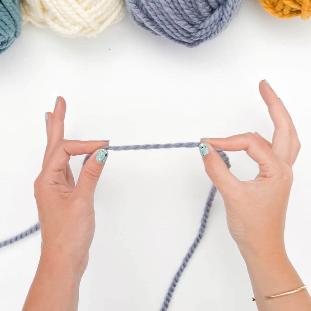 How to Tie a Slip Knot - Step 1.
A knitter's hands hold a section of yarn approximately 2" apart.