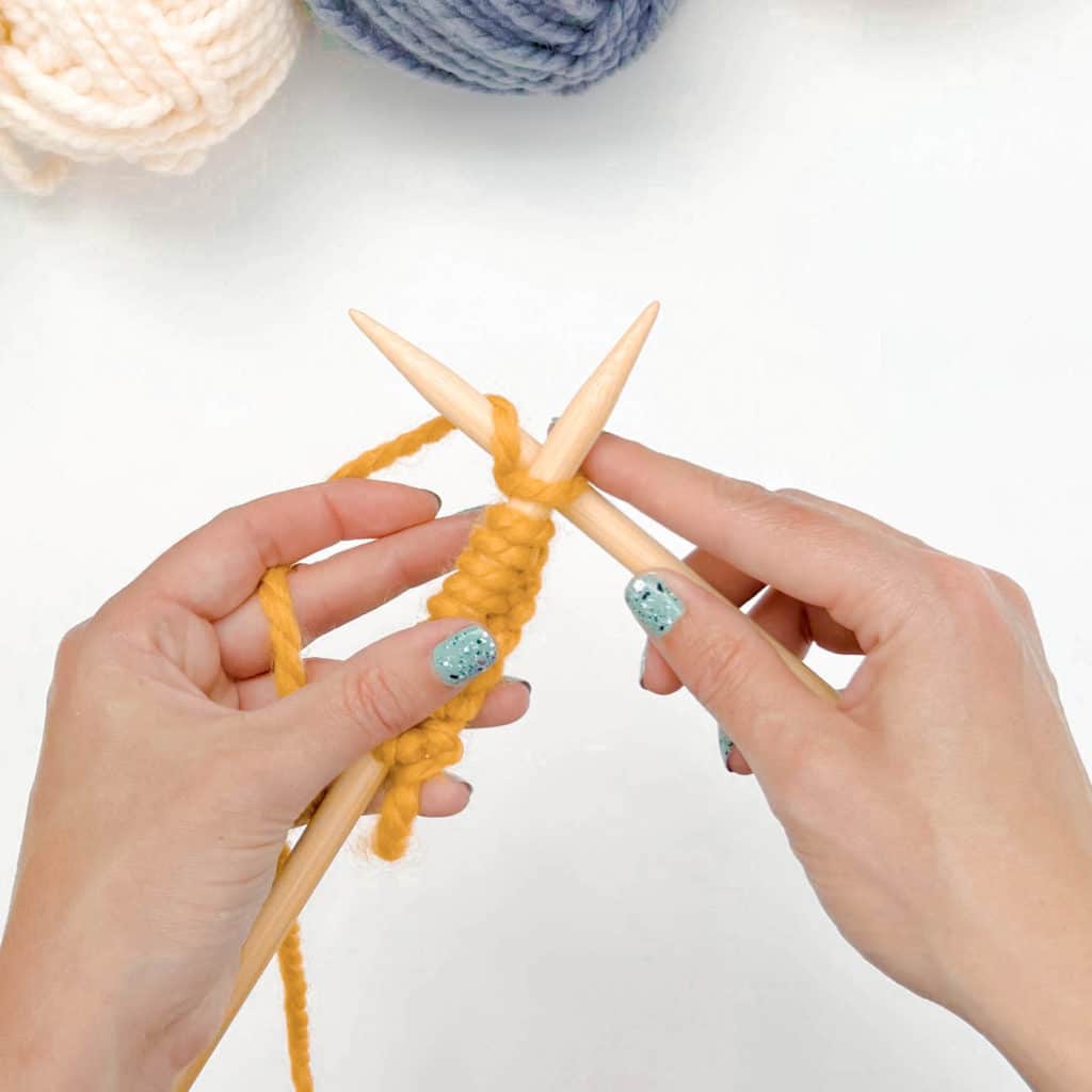 The left pointer finger brings the working yarn up and over (counter-clockwise) so that it is between both needles.