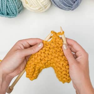 Knitter uses the left needle to bring the first stitch on the right needle over the second stitch and then drops it; leaving one stitch on the right needle.
