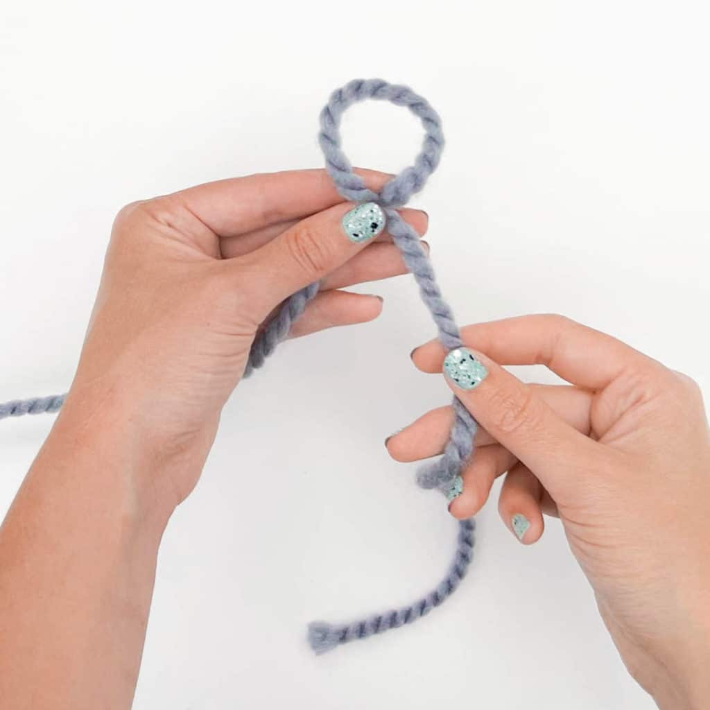 How to Tie a Slip Knot - Step 3.
One hand is used to pinch/secure the loop while the other hand holds the yarn tail