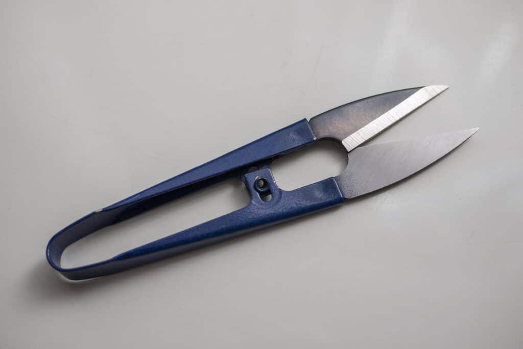 Knitting Supplies for Beginners - Blue metal u-shaped scissors for knitting, embroidery, and sewing. Sitting on a natural white background.