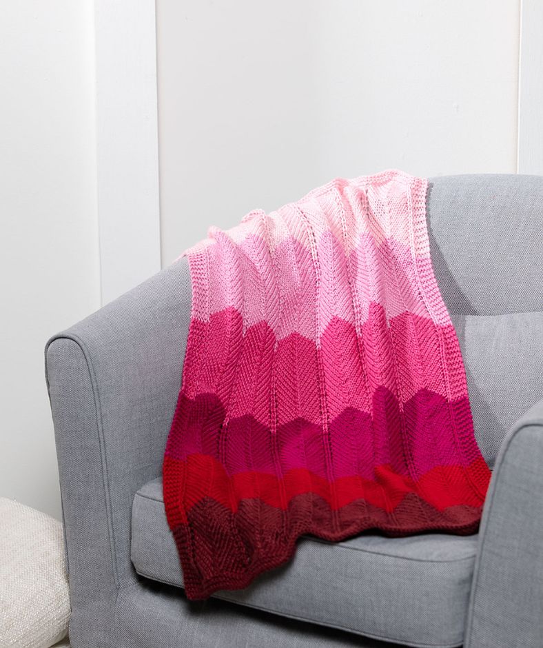 Baby Blanket Knit Patterns - Chevron Baby Knit Blanket in shades of pink and red draped over a couch in the living room