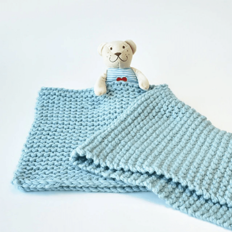 An image of a baby blanket covering a teddy bear. This pattern shows that knitting a blanket doesn't need complicated stitches.