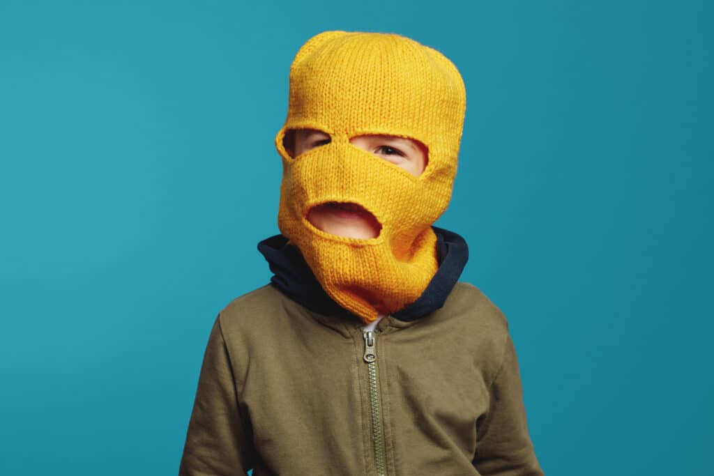 Little cute kid boy wearing yellow knitted balaclava and casual clothes. This image is showing the finished product of a free knit balaclava pattern.