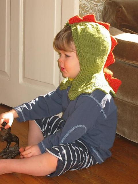 An image of a baby wearing the finished version of the Toddler Dinosaur free knit balaclava pattern.