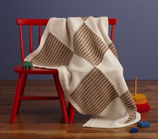 This is an image of a simple knit baby blanket draped over two chairs to show off the colorwork pattern.