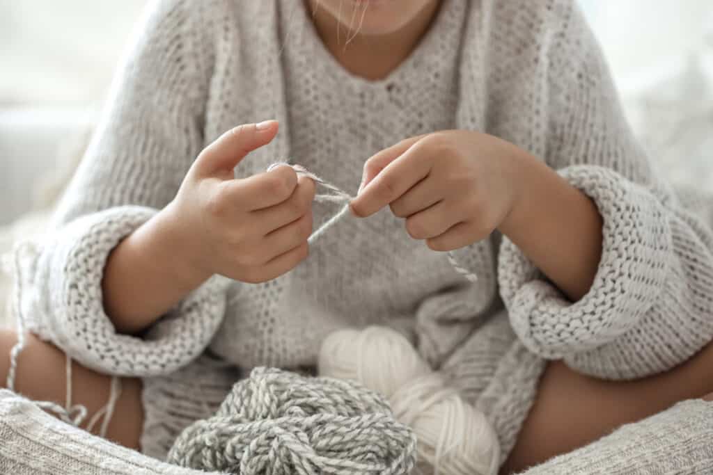 Little girl sitting on the sofa and learning how to finger knit.