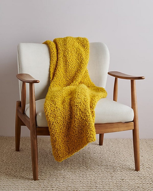 An image of a wool blanket draped over a chair. This is one of the free blanket knitting patterns in the article.