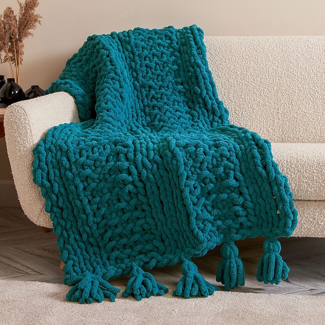 Image of a chunky blanket draped over a couch. This is a pattern showing how to make a chunky knit blanket.