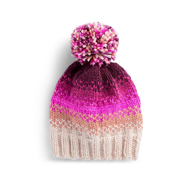 A photo of a chunky knit beanie that has a pink pompom on top. The Top of the beanie is a dark color that fades into a light shade.