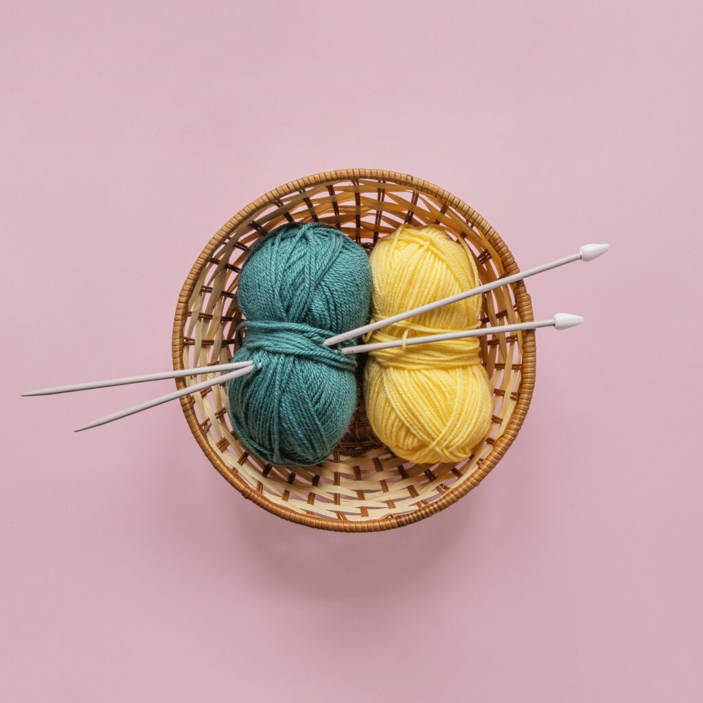Image of a bowl with two balls of yarn and a pair of knitting needles on top.