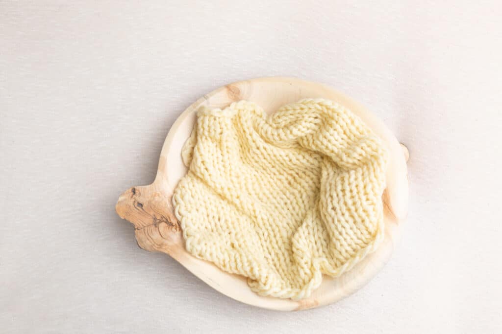 An image of a knitted fabric inside a wooden bowl. This image shows what simple knitted dishcloth patterns can look like once compelted.