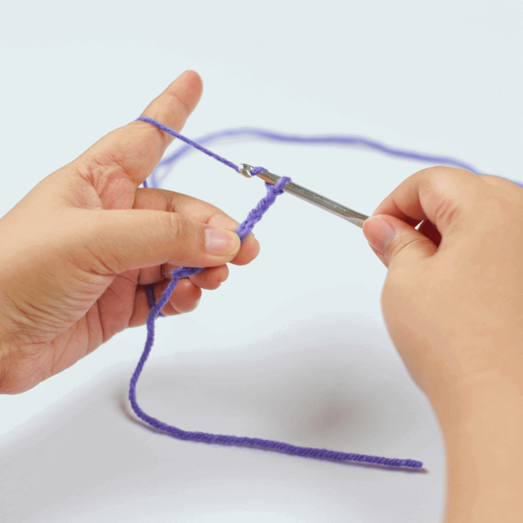 Step 2: Yarn Over

With your hook facing towards you, go under and over, grabbing the yarn like so!

(You'll notice that the chain is already quite far along in the image. This is to avoid blocking the stitch that is being worked on.)