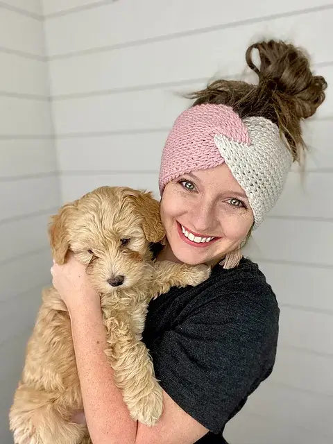 A smiling woman holding a cute puppy wearing a twisted headband made using tunisian stitches.