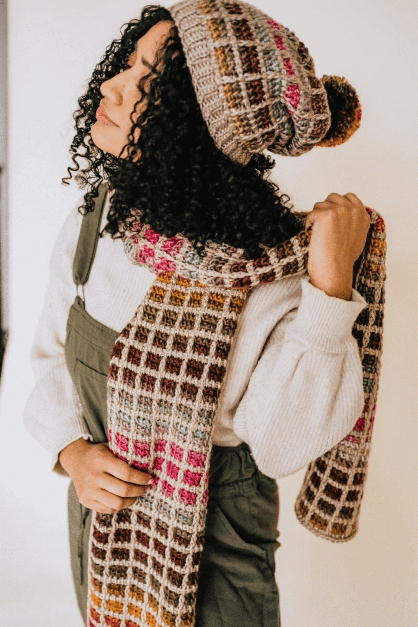 A young woman wearing a tunisian crochet beanie and tunisian crochet scarf.