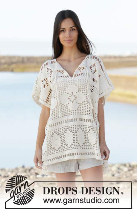 A woman wearing a crochet beach cover up top with florals and panels of filet crochet patterns all around.