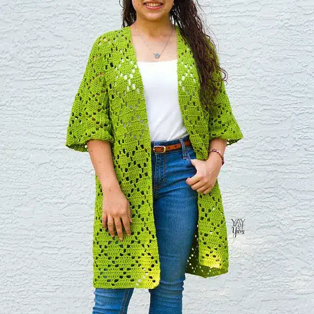 Woman wearing a bright green cardigan with diamond filet crochet patterns all over.