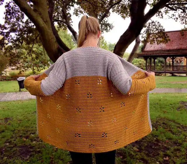 Woman with her back to the camera, wearing a crocheted cardigan with small floral filet crochet details.