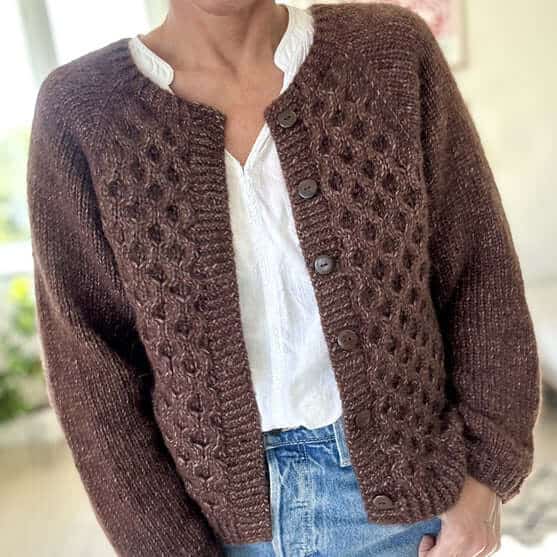 A brown, knit cabled cardigan with the buttons undone, exposing a neat white blouse.