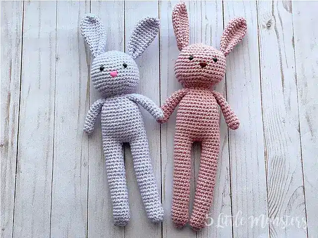 A pair of long-legged crochet bunnies laying on top of white wooden panels.