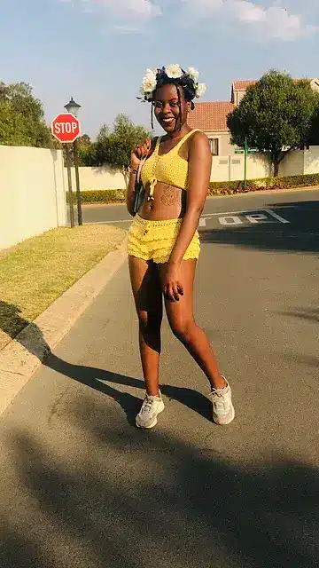 A smiling woman wearing a stunning yellow crochet shorts and top set under the sun.