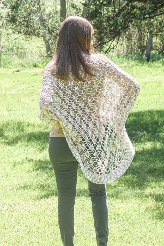 A woman with her back to the camera wearing a sheer, lace-like crochet summer shrug.