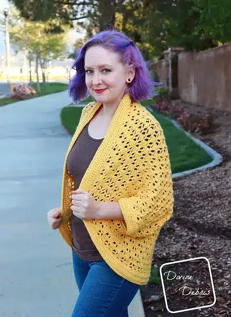A woman with light purple hair wearing an airy, butter yellow, crochet shrug.