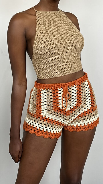 Woman wearing a pair crochet shorts made with orange, cbrown, and white yarn colors.