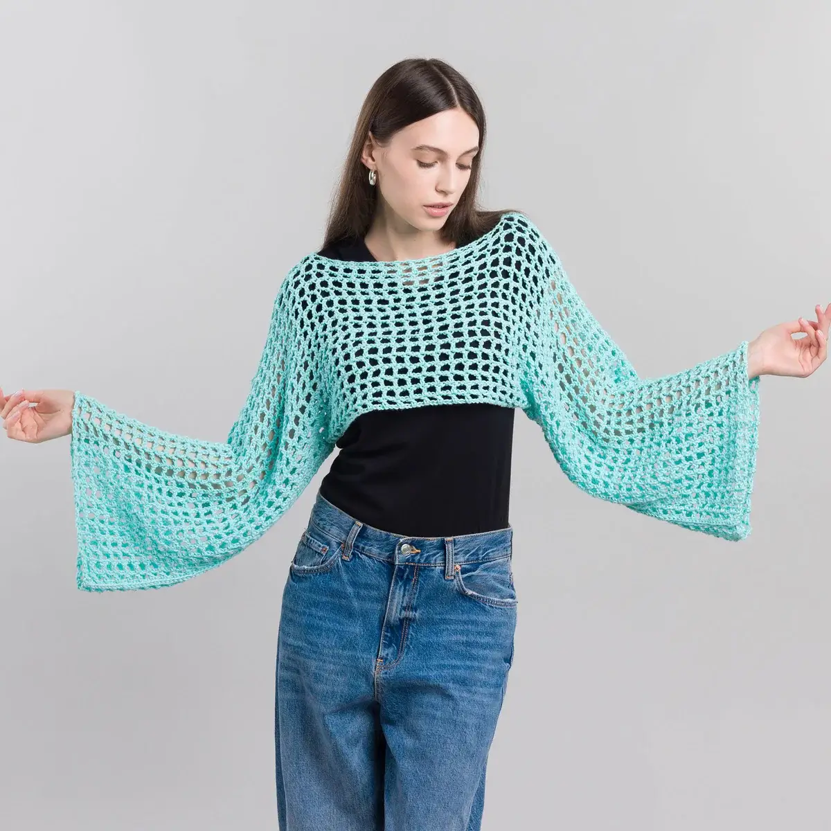 A young woman standing with her arms wide open to the sides. She's wearing a light blue crochet shrug.