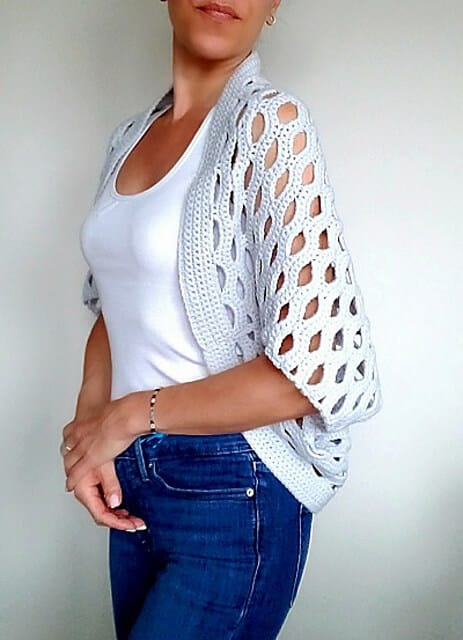 A woman wearing an airy crochet cocoon shrug and white tank top.