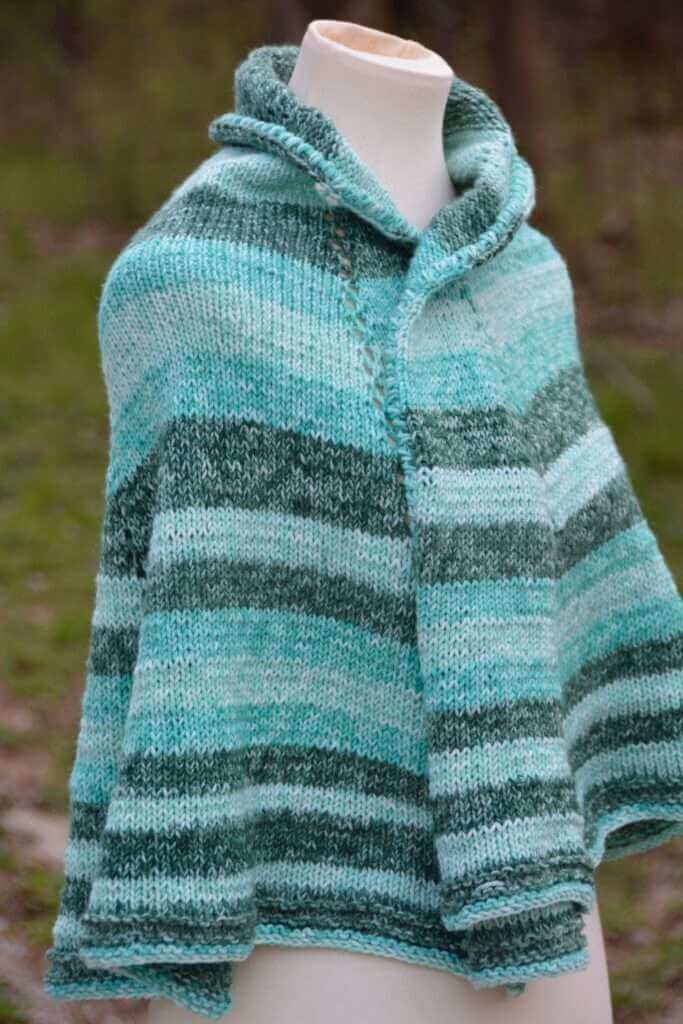 A light and flowy loom knit shawl made with blue and grey stripes draped over a mannequin.