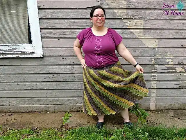 A woman wearing a long, crocheted skirt made with green, yellow, and brown yarn in a slanted pattern.